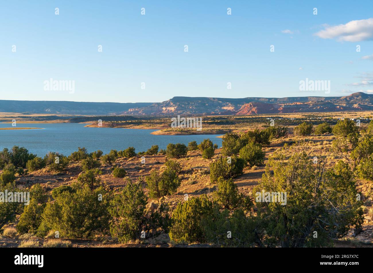 Ein Streifen blauen Sees liegt jenseits von Wacholder-bedeckten Bergrücken und einem langen flachen Mesa unter einem blassen Himmel mit einer weißen Wolke am Ghost Ranch, New Mexico. Stockfoto