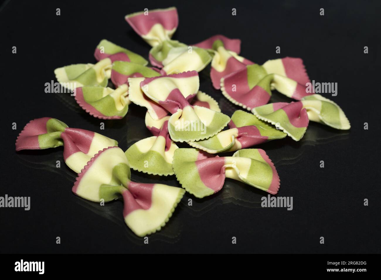 Nahaufnahme der verschütteten farbigen Pasta. Schwarzer Hintergrund mit wenig Reflexionen. Horizontale Ansicht. Werbefläche. Stockfoto