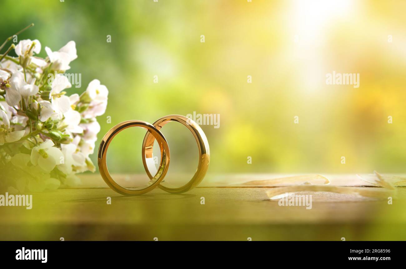 Details von zwei goldenen Ringen auf einem rustikalen Holztisch mit Blumenstrauß im Freien mit Naturhintergrund. Vorderansicht. Stockfoto