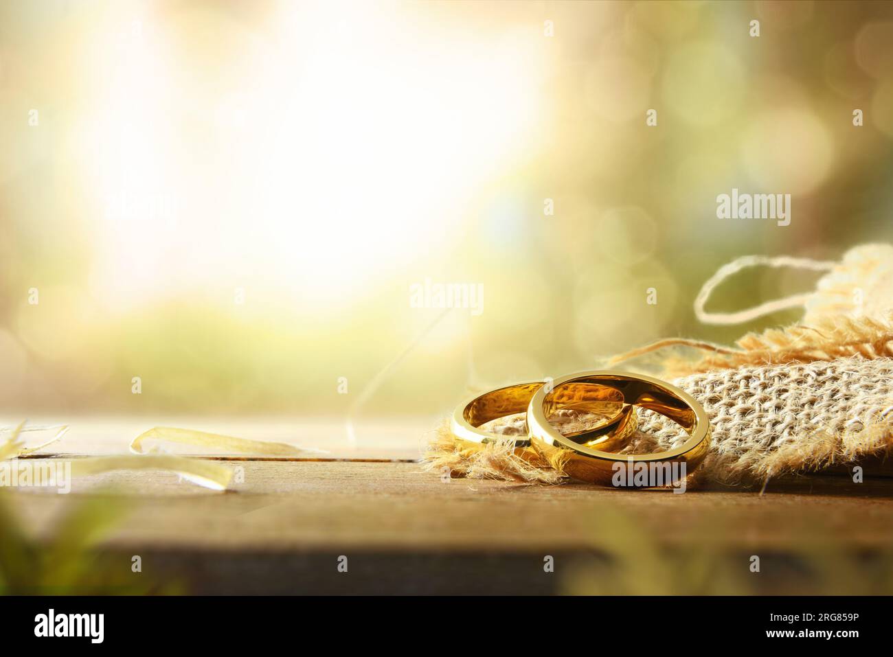Detail mit zwei goldenen Ringen auf einem Sacktuch auf einem rustikalen Holztisch und grünem Naturhintergrund mit Bokeh-Effekt. Vorderansicht. Stockfoto