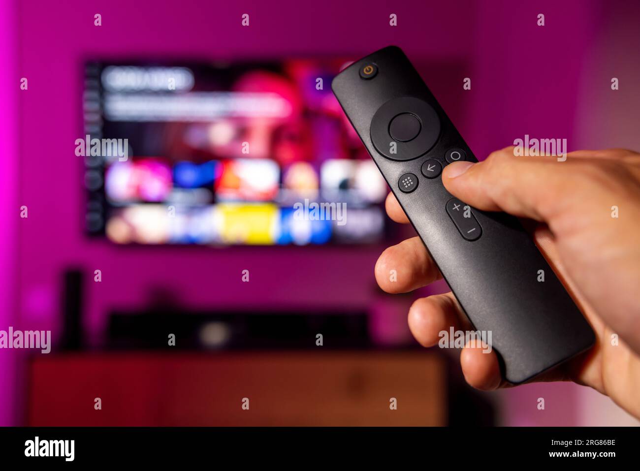 Fernbedienung in der Hand mit fernseher im Hintergrund. Streaming-Service, Content-on-Demand. Online-Fernsehen zu Hause Stockfoto