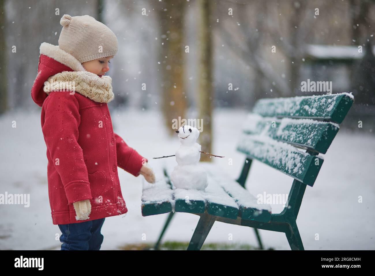 Ein bezauberndes Kleinkind, das an einem Tag mit starkem Schneefall einen Schneemann baut. Glückliches Kind, das mit Schnee spielt. Winteraktivitäten für Kinder Stockfoto