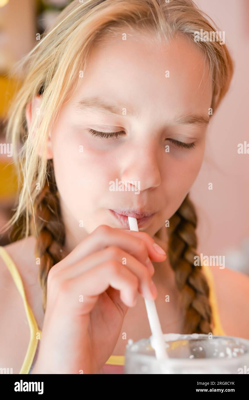 Ein hübsches Mädchen, elf Jahre alt, das Erdbeermilchshake durch einen Strohhalm trinkt, in einem Café. Portrait des glücklichen Mädchens, das einen Cocktail trinkt Stockfoto