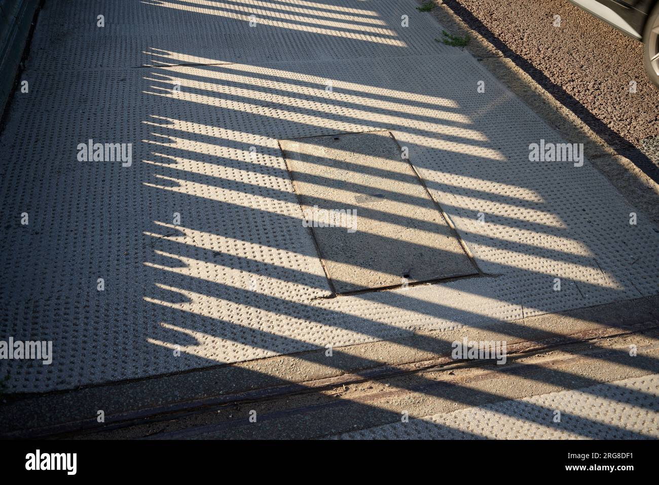 Die Textur von Licht und Schatten als geeignetes Hintergrundmuster. Sonnenlicht, das durch Geländer fließt und Schatten auf dem Bürgersteig erzeugt. Stockfoto
