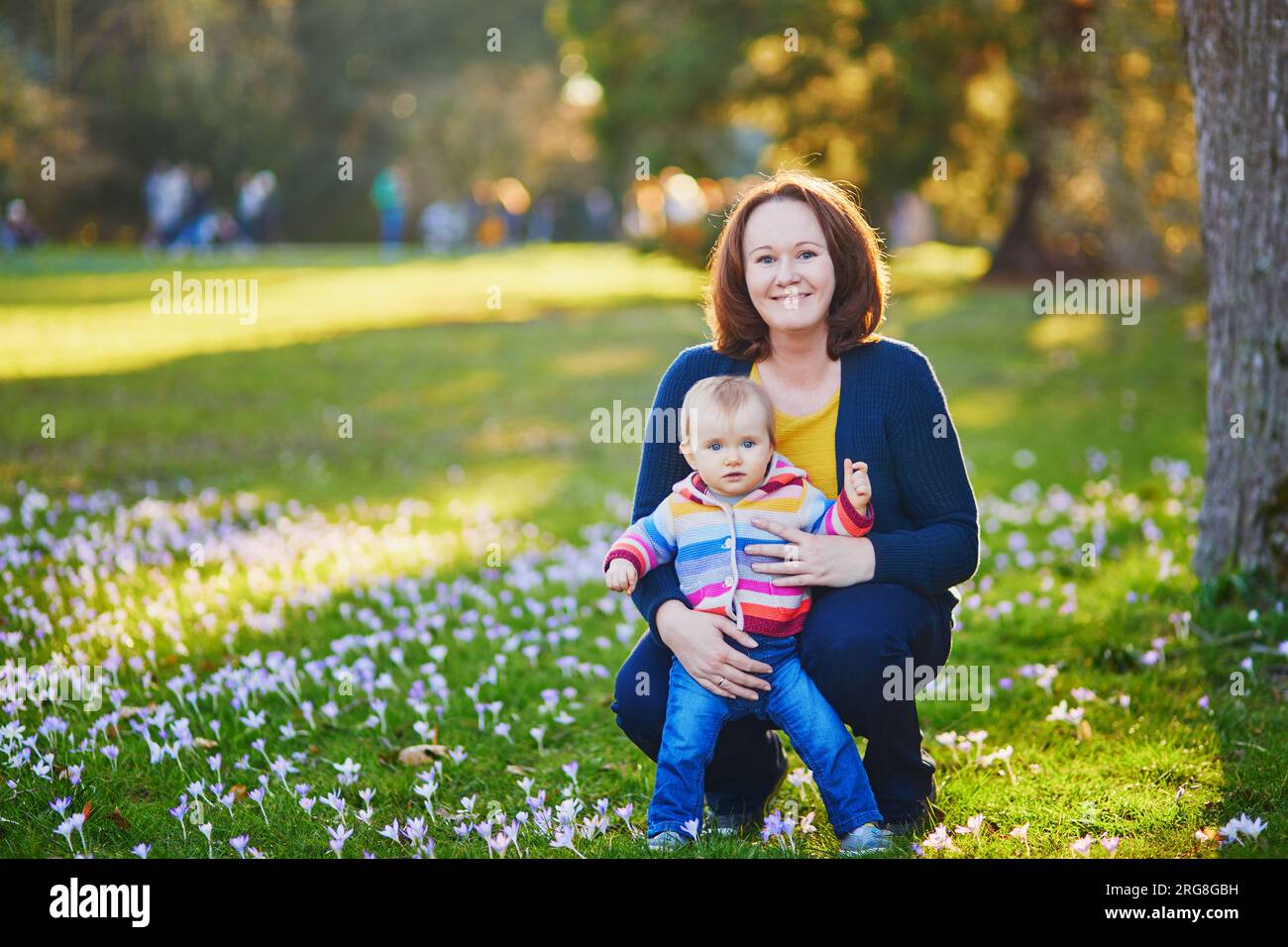 Junge Mutter mit ihrem kleinen Mädchen, die auf dem Gras mit blauen Hyazinthen saß. Familie im Freien an einem Frühlingstag Stockfoto