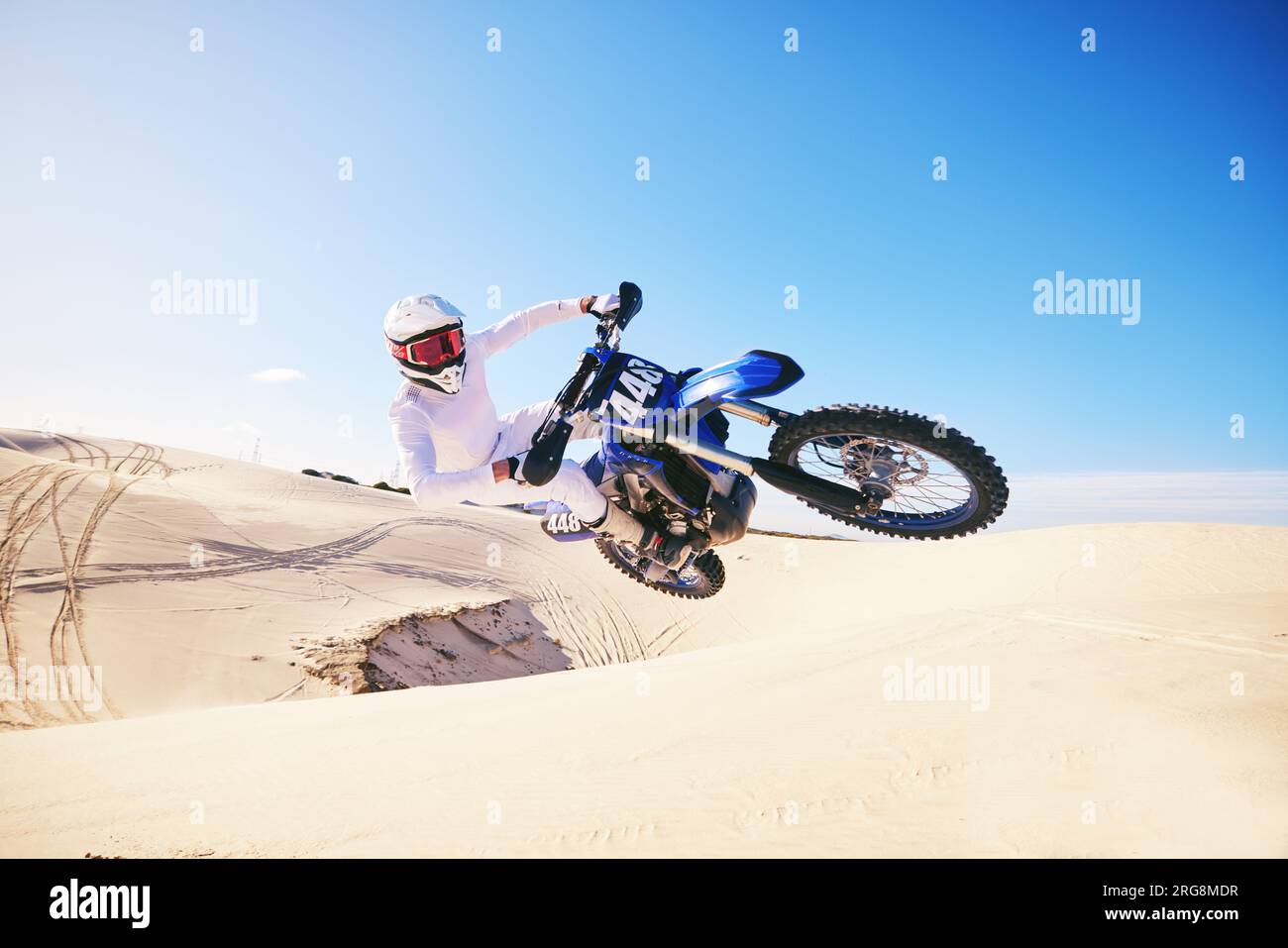 Sand, Motorsport und Mensch in der Luft mit Motorrad für Adrenalin, Abenteuer und Freiheit in der Wüste. Action, Extremsport und männlicher Fahrer auf dem Motorrad Stockfoto