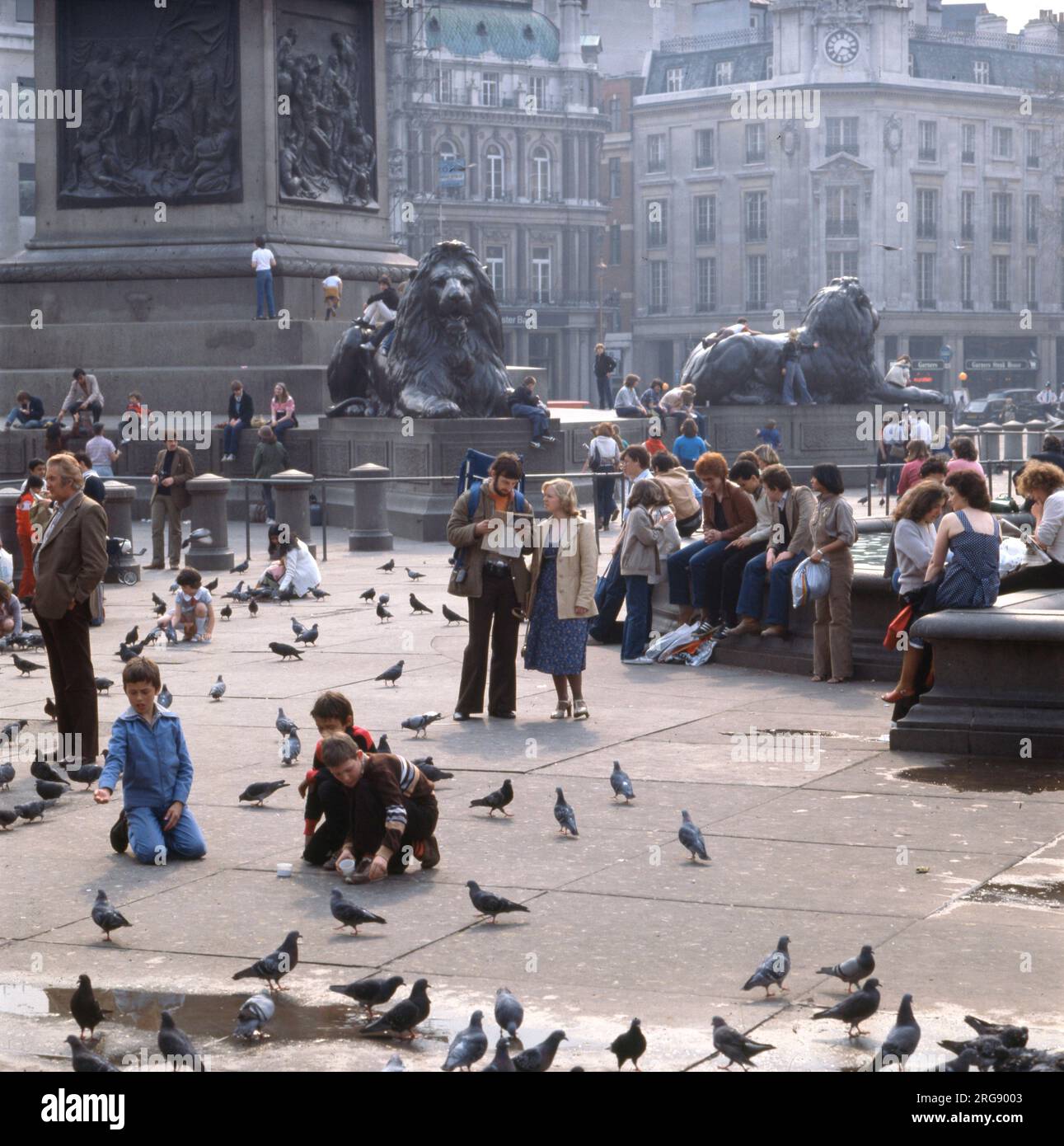 Typische Touristen füttern Tauben um Edwin Landseers Löwen am Fuße der Nelson's Column am Trafalgar Square im Zentrum von London. Stockfoto