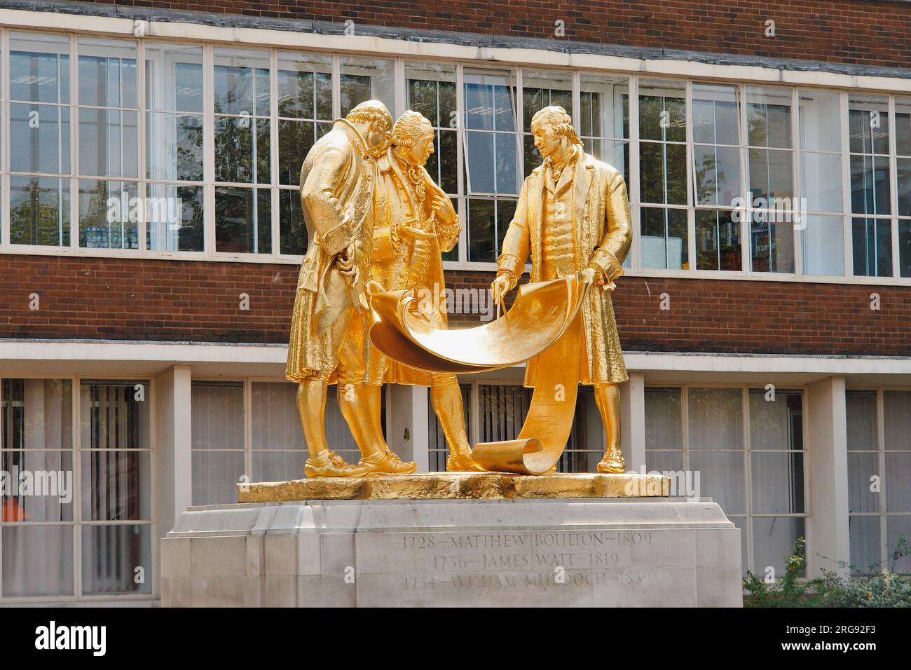Die neu vergoldete Statue von Matthew Boulton, James Watt und William Murdoch, vor dem House of Sport auf der Broad Street, Birmingham. Die Statue ist in Bronze mit goldenem Finish und stammt von William Bloye. Es wurde 1956 enthüllt. Die drei dargestellten Männer waren Pioniere der industriellen Revolution im späten 18. Jahrhundert, und es wird gezeigt, wie sie über Motorenpläne diskutieren. Die Statue hat zwei lokale Spitznamen: Die Golden Boys und die Teppichverkäufer. Stockfoto