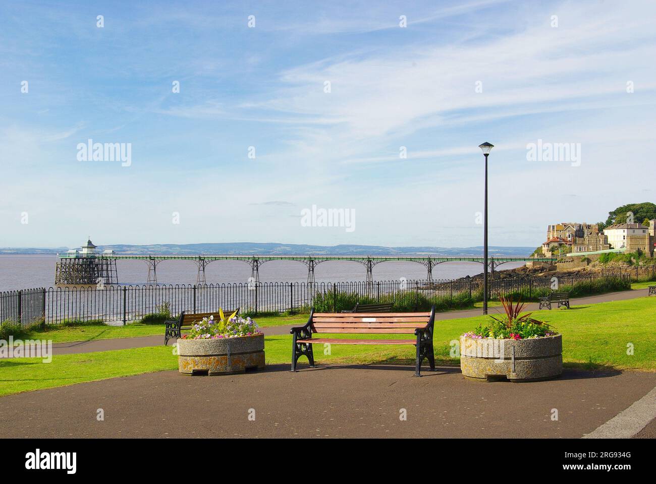 Weiter Blick auf den Pier im Badeort Clevedon in der Grafschaft Avon, mit einer Bank und Blumenwannen im Vordergrund. Der Pier wurde 1869 eröffnet. Seitdem wurden zahlreiche Reparatur- und Restaurierungsarbeiten durchgeführt, und der Pier ist nun ein Gebäude der Kategorie I. Stockfoto