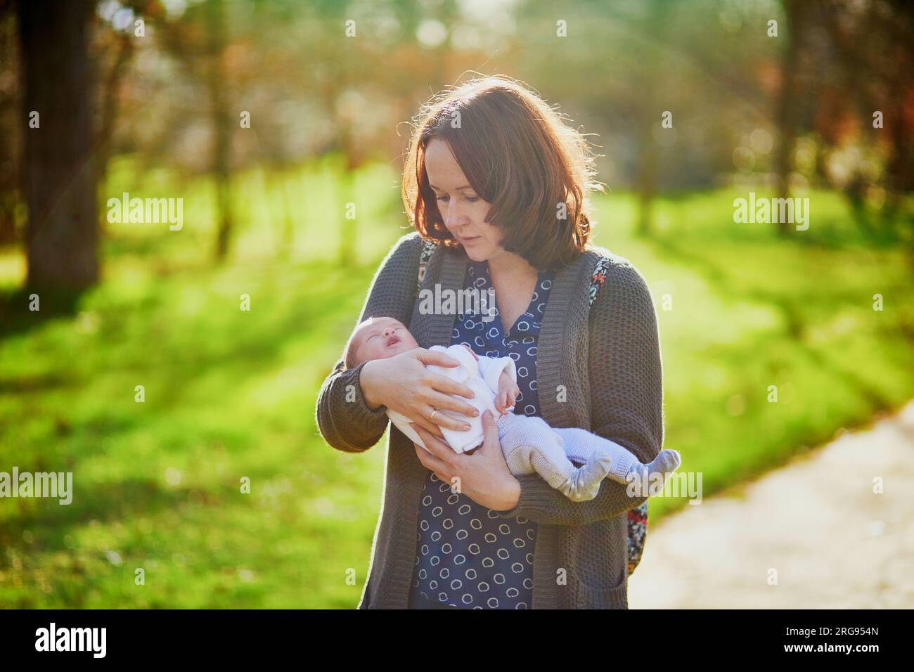 Mutter hält ein 4 Wochen altes Mädchen in den Armen. 1 Monate altes Kind in Mamas Händen im Freien. Der erste Spaziergang für ein Neugeborenes Stockfoto