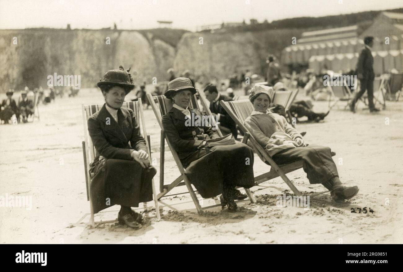 Drei Spinsters genießen die Sommersonnen am Strand von Broadstairs, Kent mit Strandhütten im Hintergrund. Stockfoto