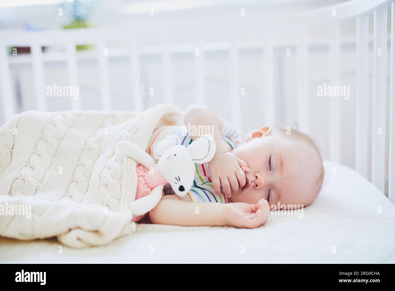 Ein bezauberndes Mädchen, das in einem Babybett schläft, das mit Plüschspielzeug am Bett der Eltern befestigt ist. Ein kleines Kind schläft einen Tag im Kinderbett. Das Schlaftrainingskonzept Stockfoto