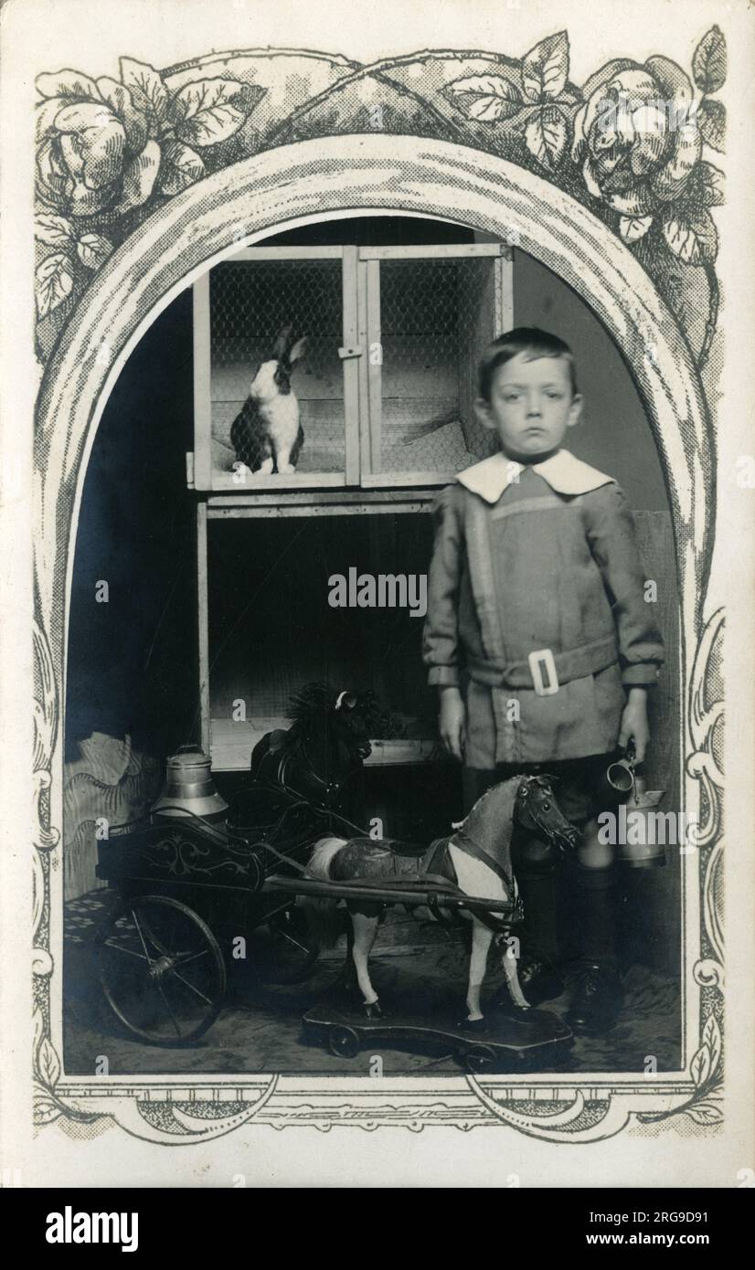 Edwardian Boy mit Spielzeugpferd und -Wagen, Großbritannien. Er steht vor einem Kaninchenstall. Stockfoto