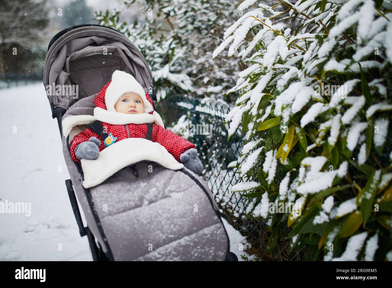 Glückliches lächelndes Mädchen im Kinderwagen in Paris Tag mit schwerem Schnee. Das kleine Kind genießt den ersten Schnee. Ungewöhnliche Wetterbedingungen in Franc Stockfoto