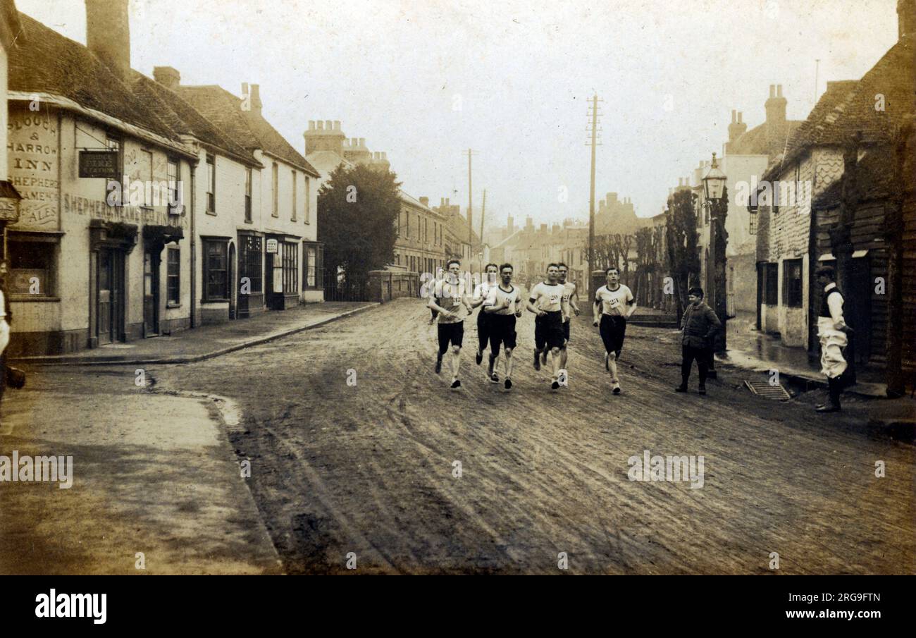 Rennen - Männer laufen (zeigt The Plough & Harrow Inn), High Street, Bridge, Canterbury, Kent, England. Stockfoto