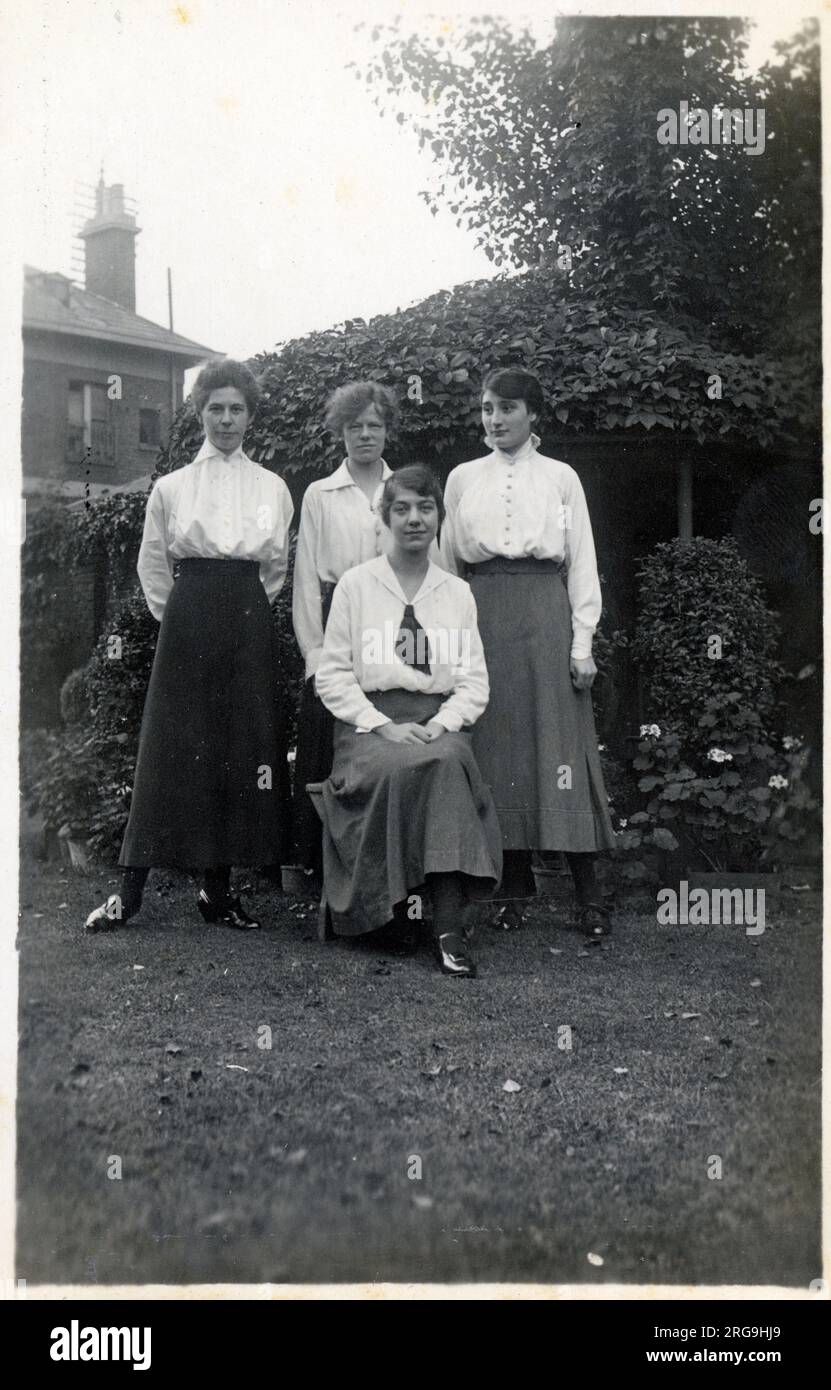 Vier Studentenfreunde posieren für ein Gruppenfoto auf dem Rasen eines Vorstadtgartens. Stockfoto