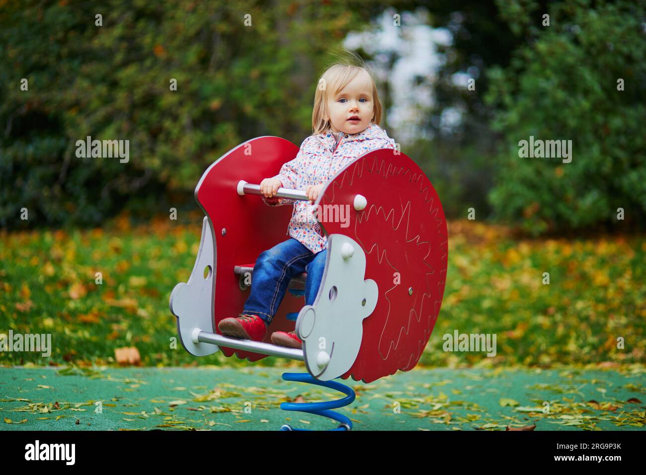 Ein bezauberndes Kleinkind, das Spaß auf dem Frühlingsreiter auf dem Spielplatz hat. Aktivitäten im Freien für Kinder Stockfoto