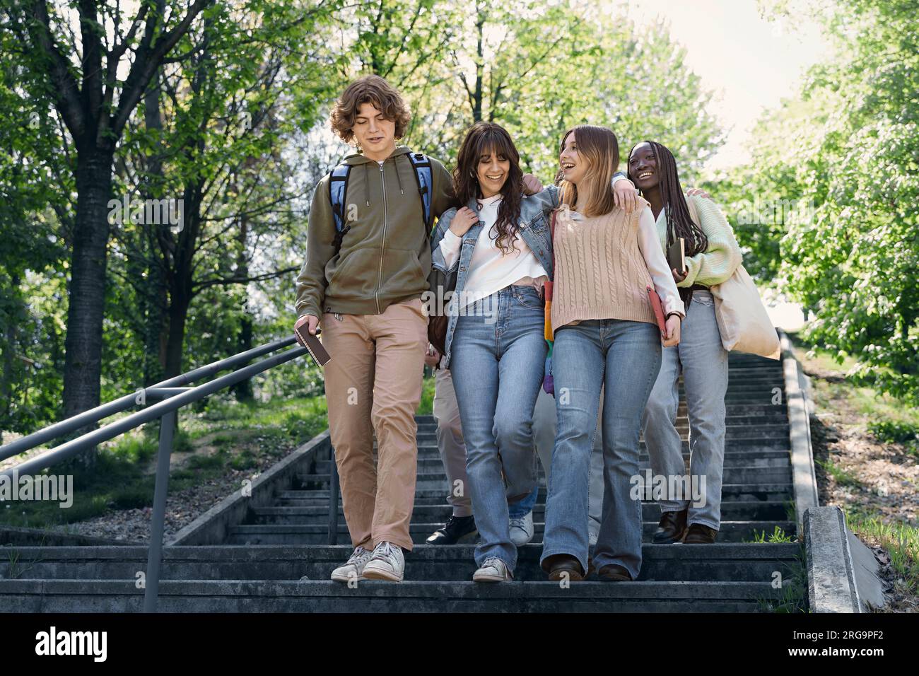 Eine Gruppe verschiedener Teenager mit Rucksäcken und Notizbüchern konversieren sich, wenn sie die Parktreppe hinuntersteigen, die von der Hüfte nach oben eingefangen wird. Wir haben einen lebhaften Betrug Stockfoto