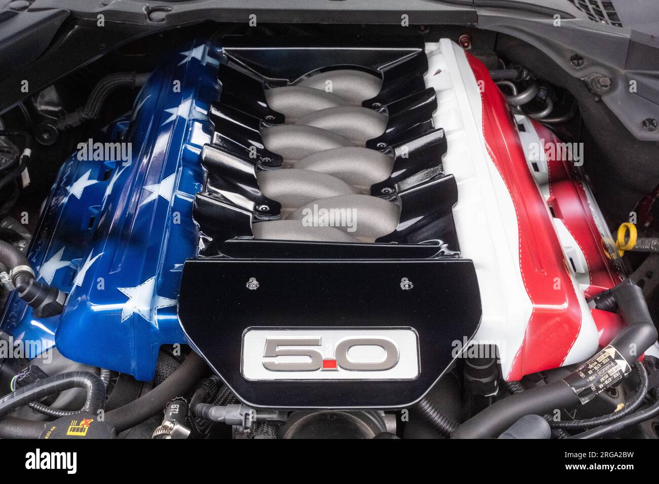 Der Motorraum eines amerikanischen Ford Mustang mit 5,0 Litern Hubraum und den Stars and Stripes auf dem Motorblock. Stockfoto