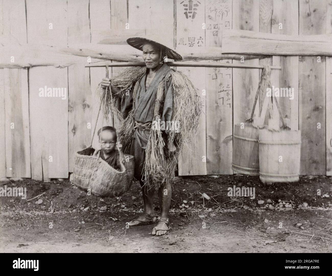 Japanischer Bauer Mann, der Kind in einem Korb trägt. Vintage 19. Jahrhundert Foto. Stockfoto