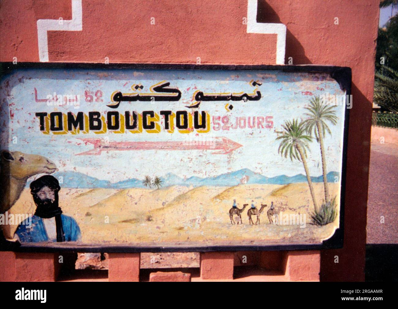 Ein handgemaltes Schild zeigt die Zeit, die man braucht, um Timbuktu in Mali zu erreichen (52 Tage), wenn man auf einem Kamel durch die Sahara fährt! Ein Beduinenmann aus Mali Tuareg ist unten links auf dem Schild abgebildet Stockfoto