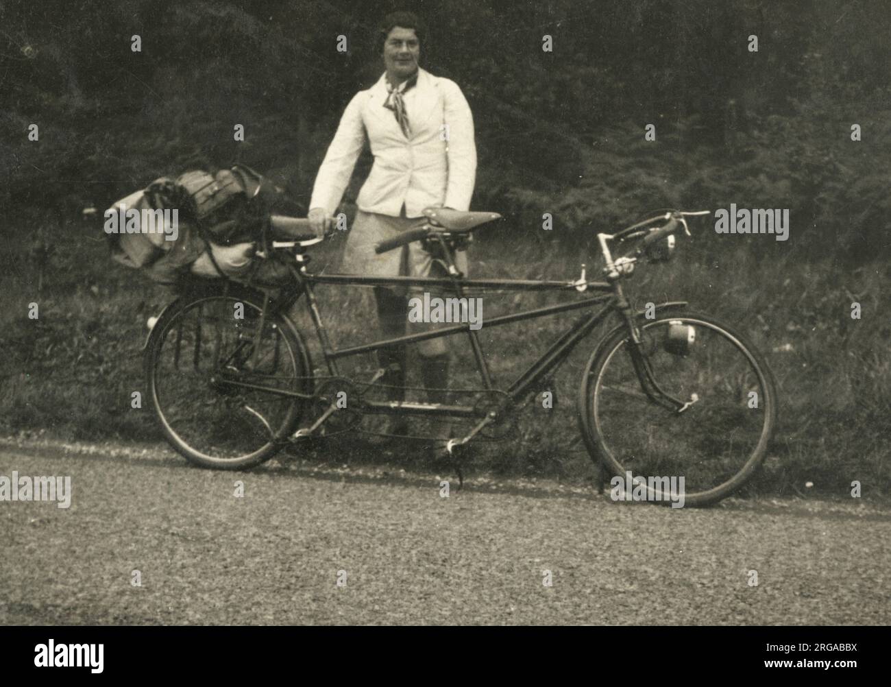 Eine Dame, die für eine Radtour vorbereitet ist, in warmen Mänteln und langen Socken, die neben einem großartigen Fahrrad für zwei stehen, das mit Zelt und Gegenständen beladen ist. Stockfoto