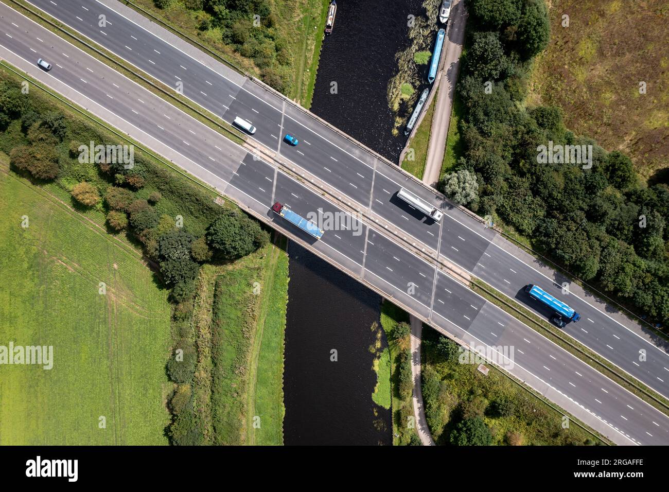 Luftaufnahme direkt über einer geschäftigen britischen Autobahn, die über einen Fluss oder eine Kanalbrücke auf dem Land führt Stockfoto