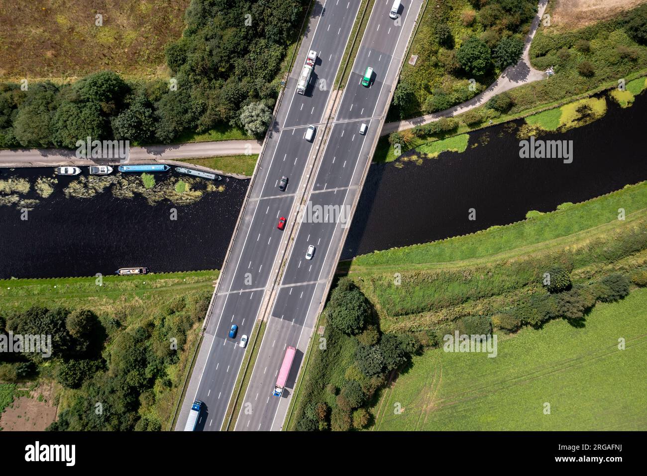Luftaufnahme direkt über einer geschäftigen britischen Autobahn, die über einen Fluss oder eine Kanalbrücke auf dem Land führt Stockfoto