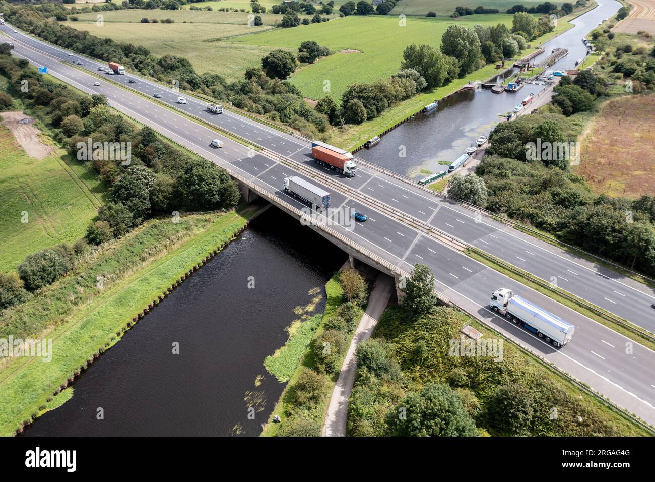 Luftaufnahme direkt über einer geschäftigen britischen Autobahn, die einen Fluss oder eine Kanalbrücke auf dem Land überspannt Stockfoto