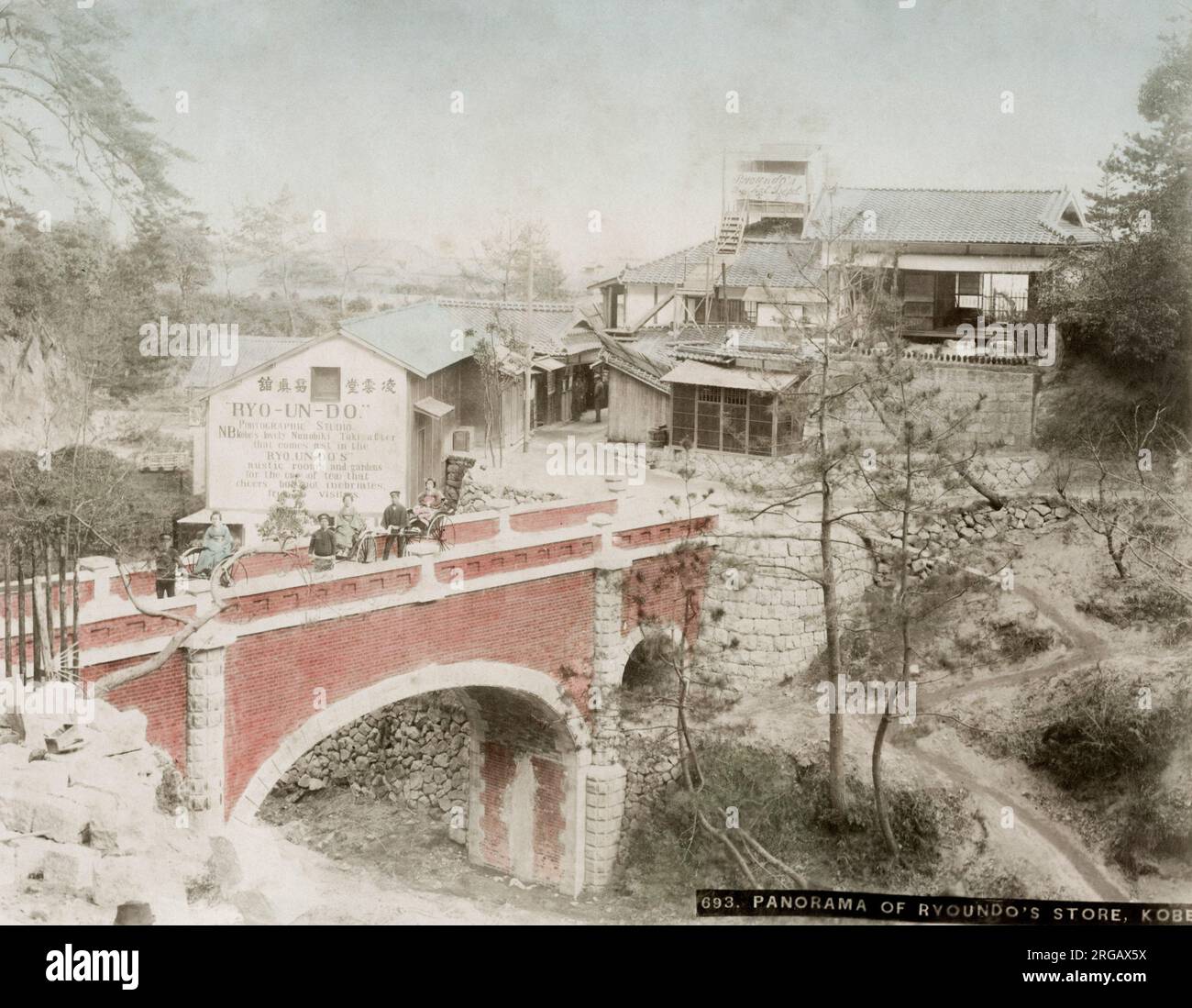 Vintage-Fotografie aus dem 19.. Jahrhundert: Brücke- und Straßenszene in der Nähe von Kobe, mit großem Werbeschlag für das Fotostudio Ryo-UN-do, das großformatige Bilder japanischer Szenen und Menschen an westliche Touristen und Reisende verkaufen würde. Bild, ca. 1890 Stockfoto