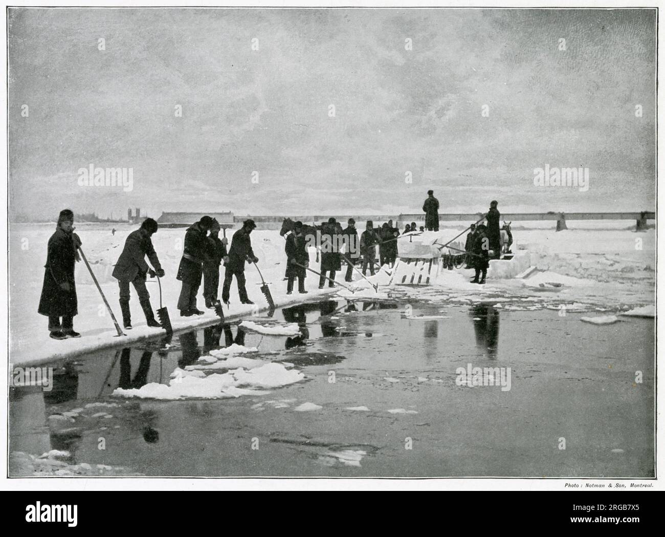 Eine Gruppe, die in den Wintermonaten Eis in Platten in gefrorenen Seen bei Montreal, Kanada, zerlegt. Im Hintergrund befindet sich die große Brücke, die die transkontinentale Strecke der Canadian Pacific Railway befährt. Stockfoto
