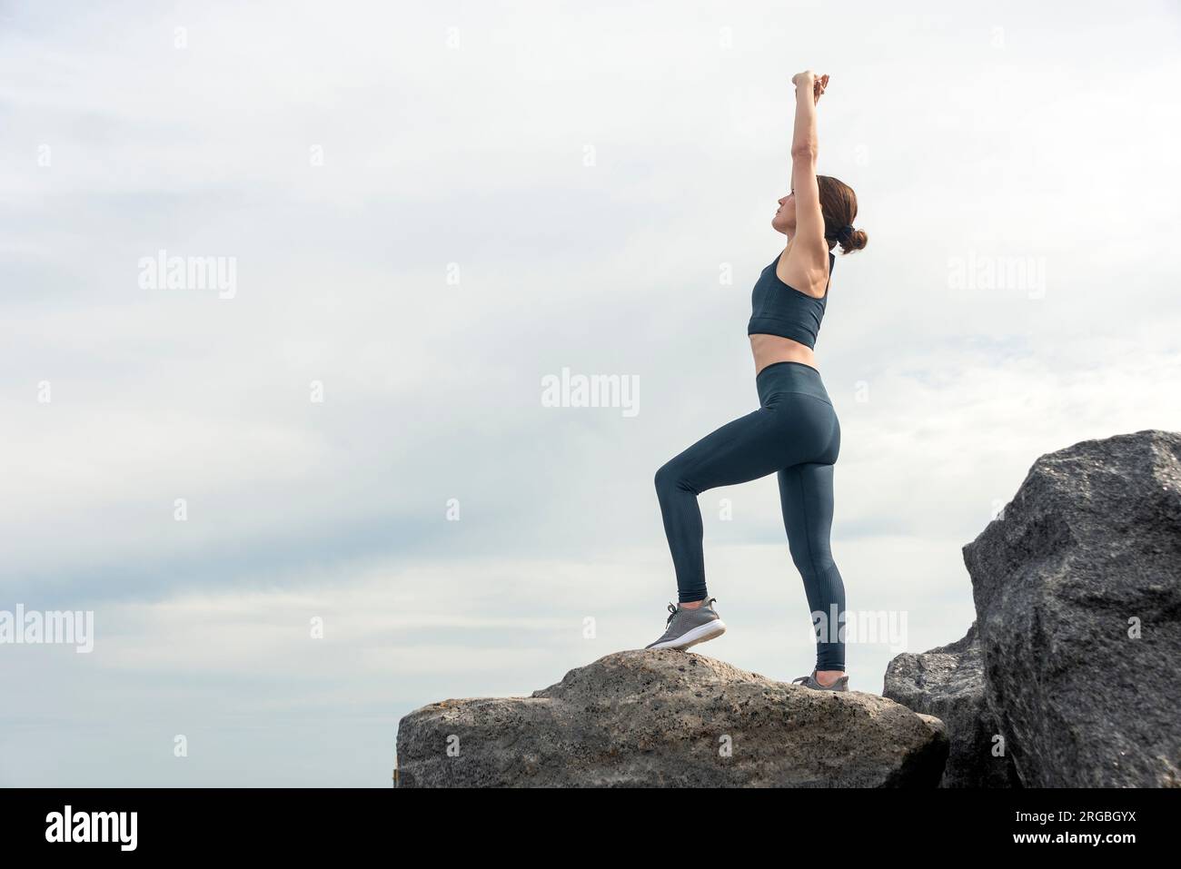 Seitenansicht einer sportlichen Frau, die draußen auf Felsen und Felsbrocken steht und eine Dehnübung macht. Stockfoto