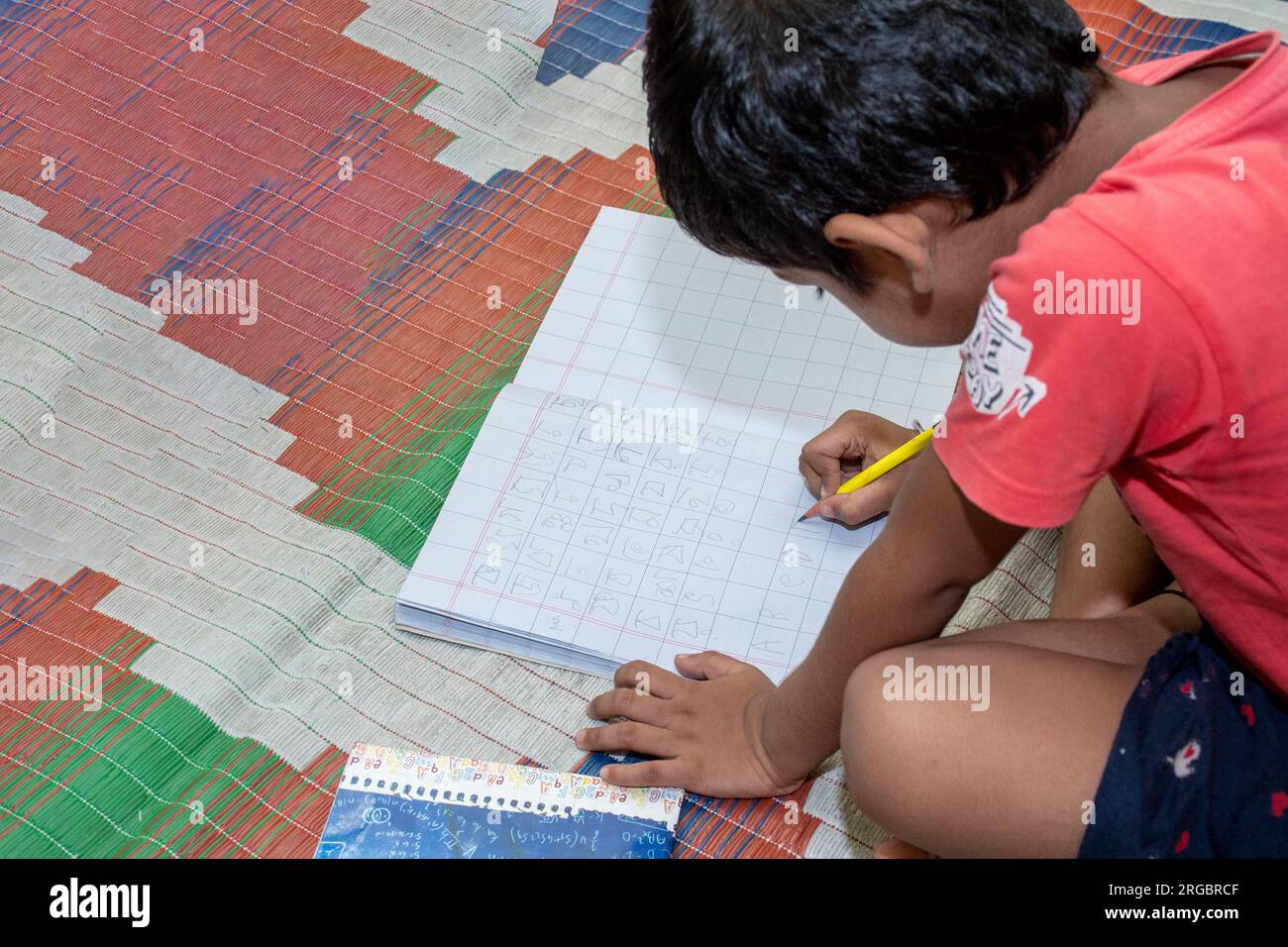 Ein Kind auf dem Land liest und schreibt mit einer Konzentration auf Selbstentwicklung, die allein auf einer Matte liegt Stockfoto