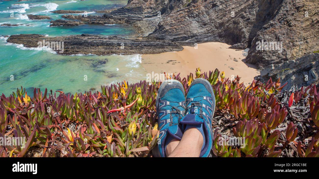 Trekkerfüße, die auf dem Rand der Klippe ruhen. Küste von Cabo Sardao, Ponta do Cavaleiro, Sao Teotonio, Portugal Stockfoto