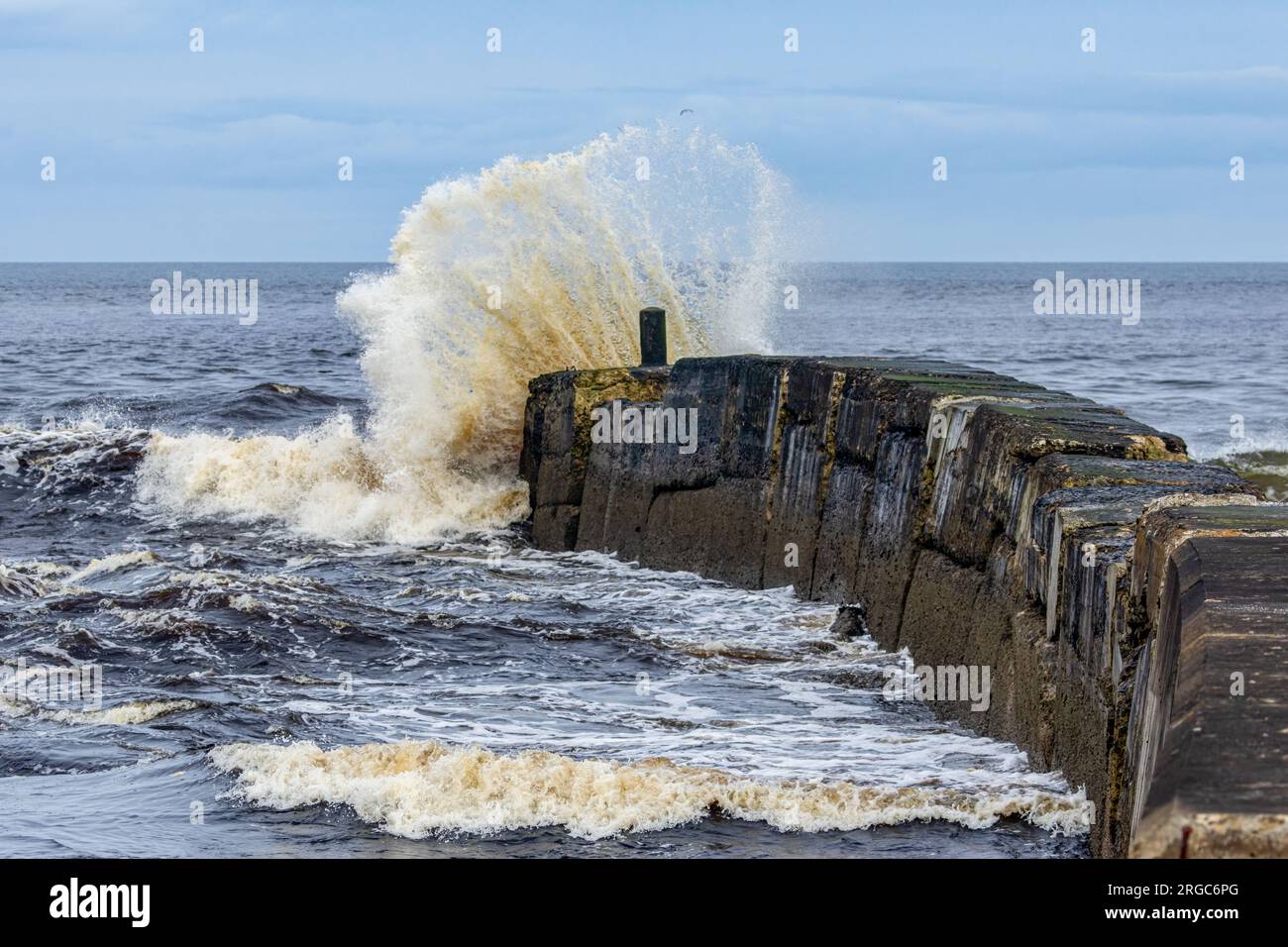 Große Welle während eines Sturms, der über eine alte Hafenmauer an der Küste kommt Stockfoto