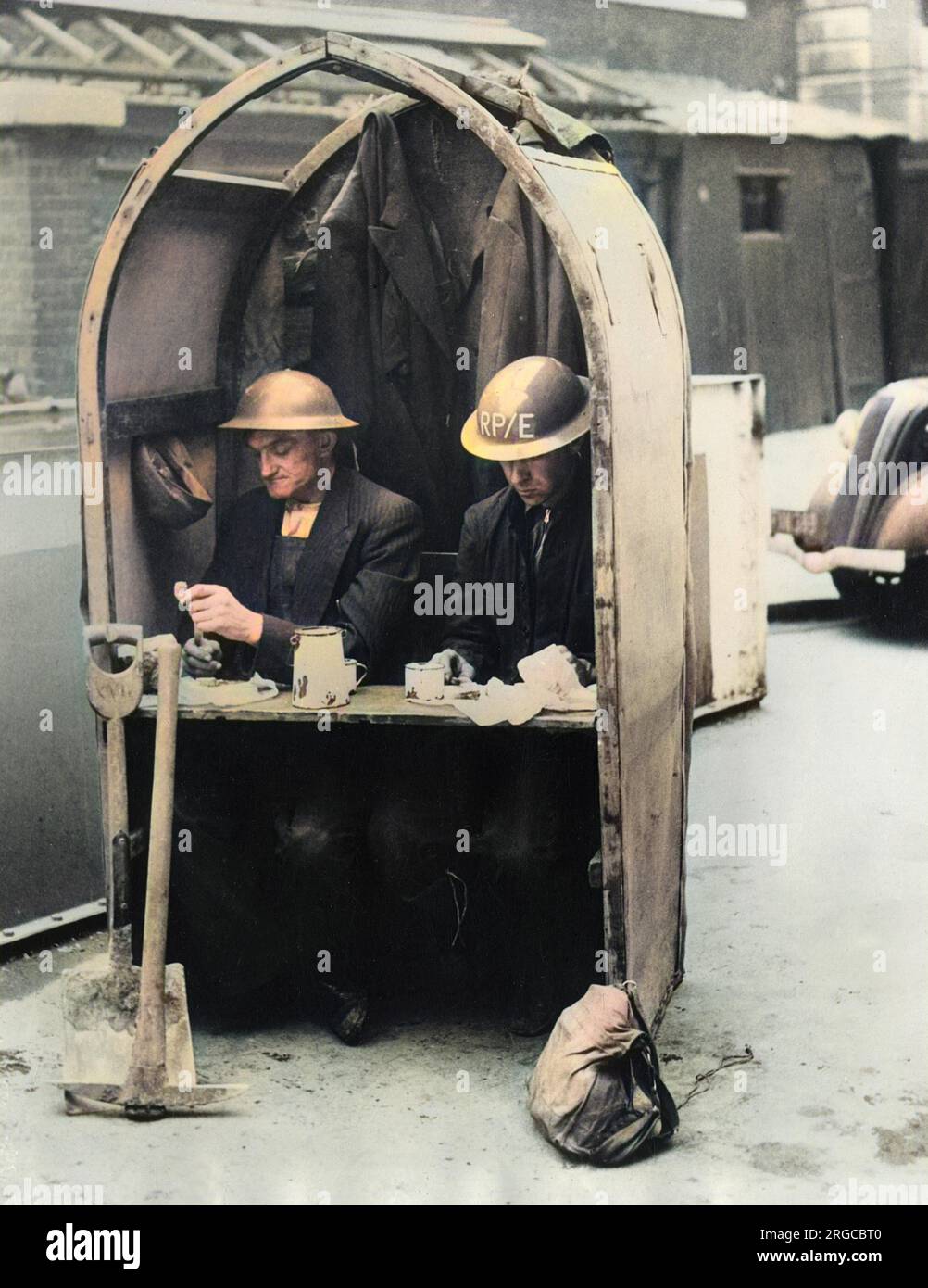 Bleib ruhig und mach weiter. Ein ziemlich fantastisches Foto, auf dem zwei Arbeiter gezeigt werden, die an der Reparatur von Schäden durch Luftangriffe in der Londoner Gegend beteiligt sind, setzen ihr „privates“ Mittagessen fort, obwohl die Sirenen eine weitere „Alarmstufe“ ausgelöst haben - Oktober 1940. Stockfoto