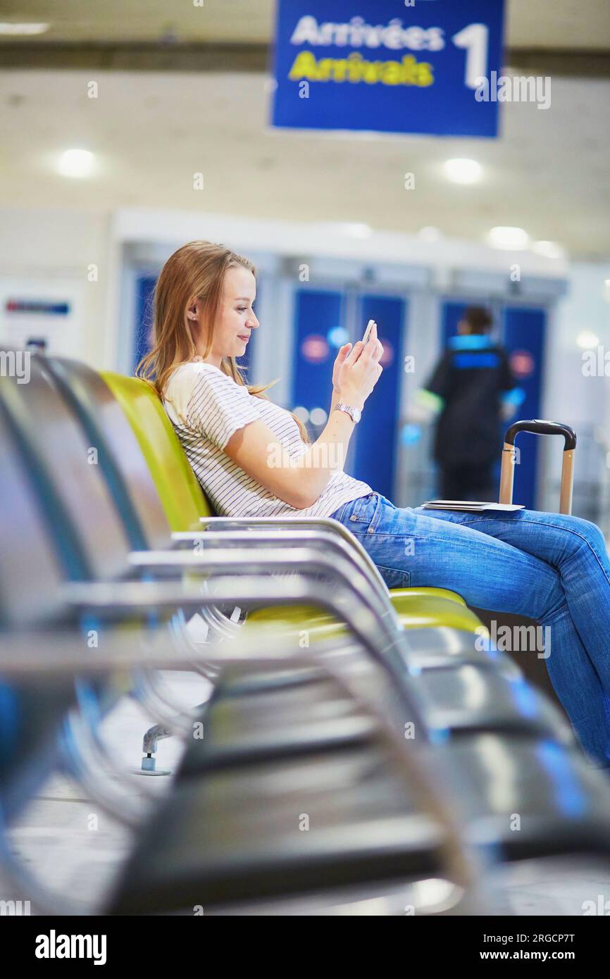 Junge Reisende mit Handgepäck im internationalen Flughafen, die auf ihren Flug warteten und ihr Handy überprüften Stockfoto