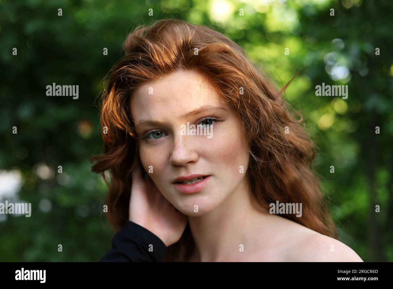 Porträt eines lächelnden Ingwermädchens mit langen roten Haaren und Sommersprossen im Sommerpark. Ein junges sinnliches Modell, das in die Kamera schaut Stockfoto