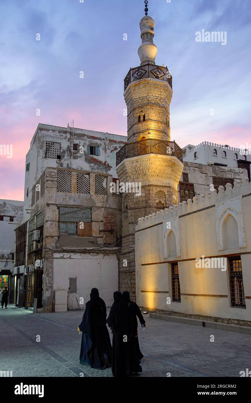 Muslimische Frauen in schwarzen Abayas gehen bei Sonnenuntergang an der Al Shafi Moschee vorbei, der ältesten Moschee in Al-Balad, Dschidda, Saudi-Arabien. Stockfoto