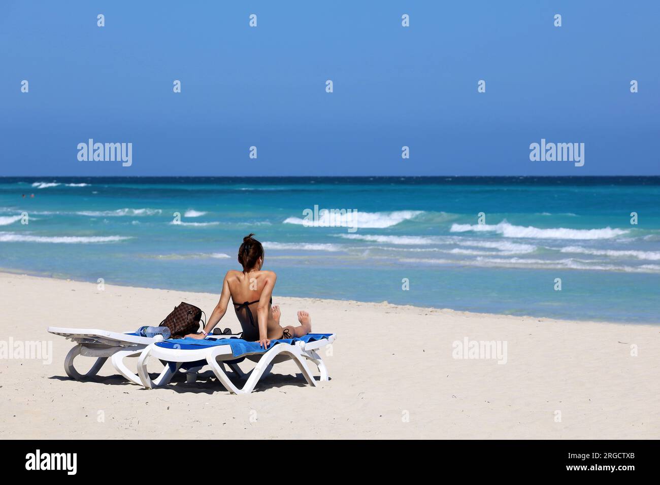 Ein Mädchen im Badeanzug, das sich auf dem Liegestuhl bräunt, mit Meereswellen im Hintergrund. Strand mit weißem Sand an der Küste des Ozeans Stockfoto