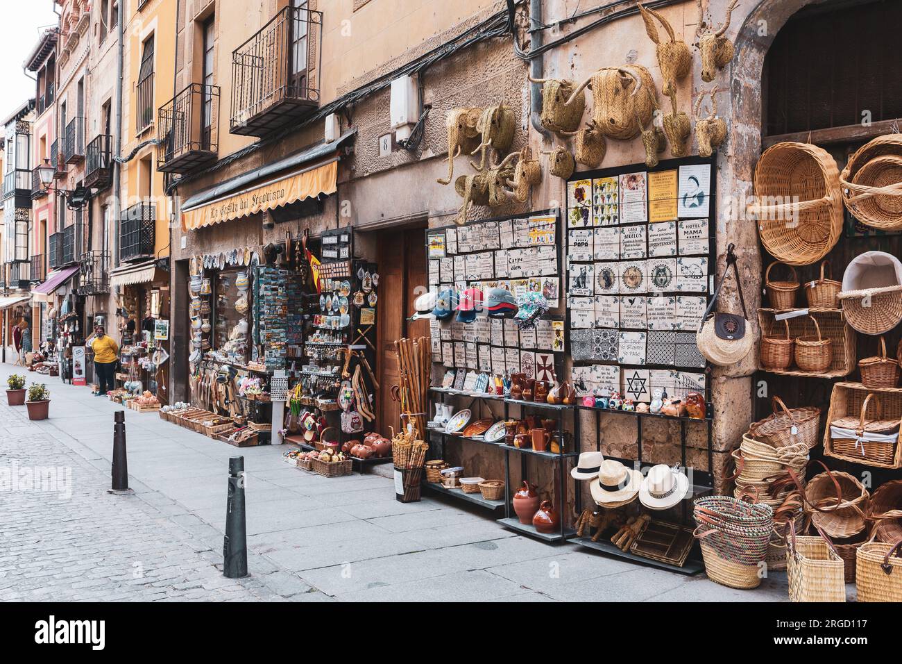 Segovia, Spanien, 03.10.21. Souvenirladen in einer schmalen mittelalterlichen Straße mit Korbkörben, Hüten, dekorativen Fliesen, Magneten und Töpferwaren. Stockfoto