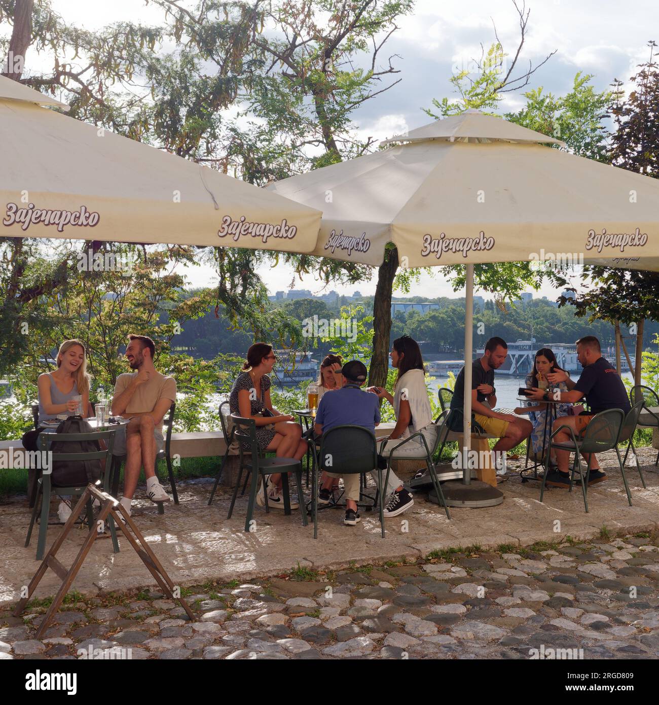 Gäste in einem Café/Restaurant auf einer Kopfsteinpflasterstraße an einem Sommertag mit Blick auf die Save in Belgrad, Serbien. August 8,2023. Stockfoto