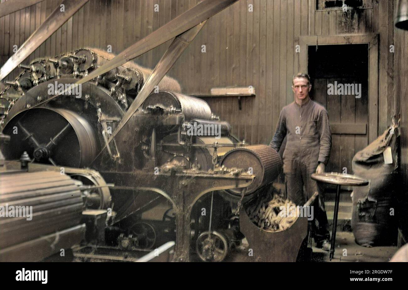 Ein Mann in der Textilindustrie in Schottland, der eine Maschine mit vielen Rollen bedient. Stockfoto