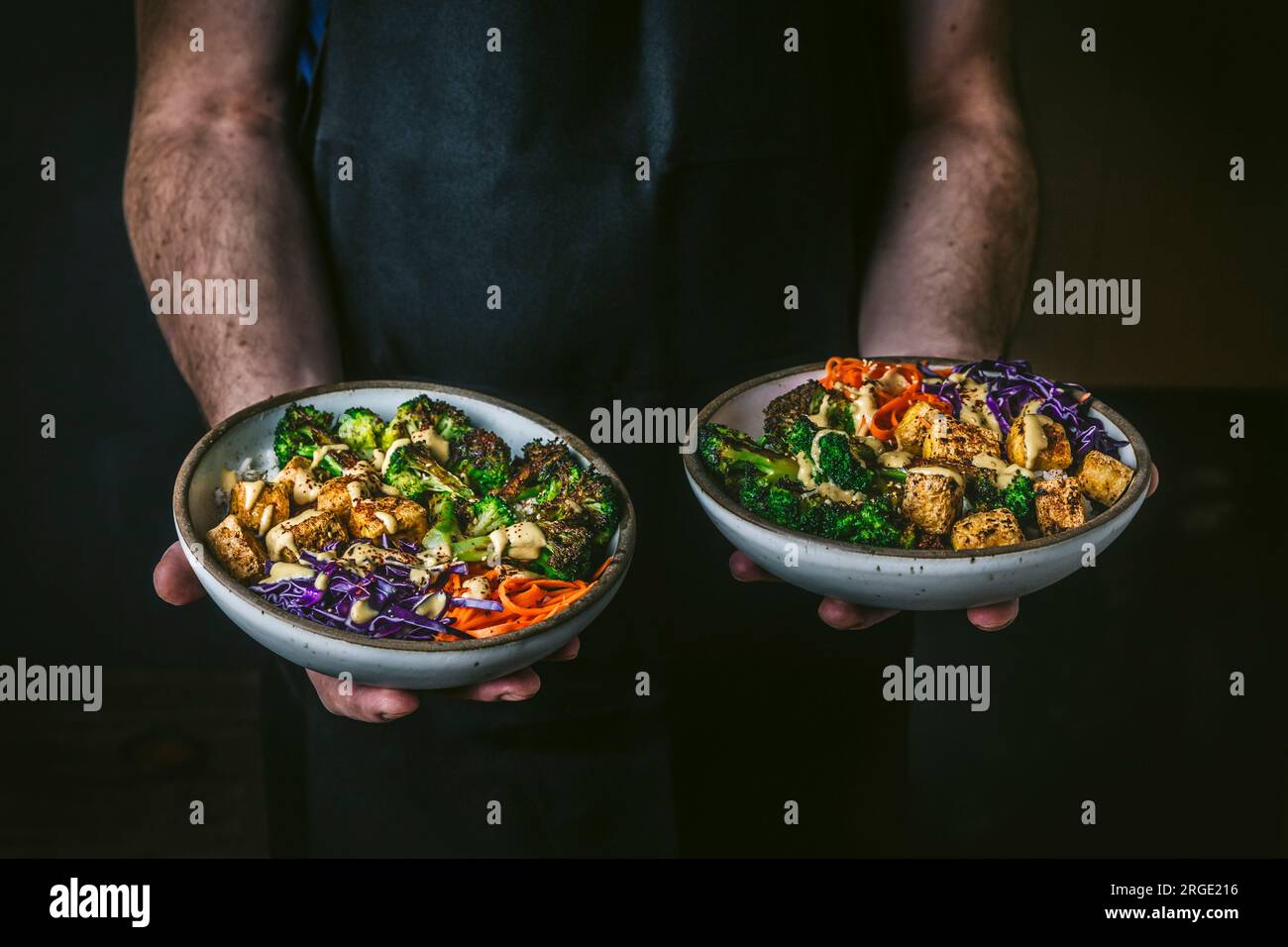 Mann mit 2 Schüsseln gefüllt mit geröstetem Brokkoli, Tofu und bunten Gemüse mit dunklem Hintergrund Stockfoto