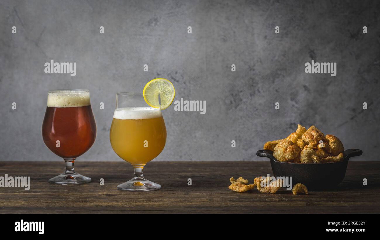 Eine Weizenschale und ein braunes Ale, in Tulpengläsern auf einem Holztisch mit Schüssel mit Schweineschale Stockfoto