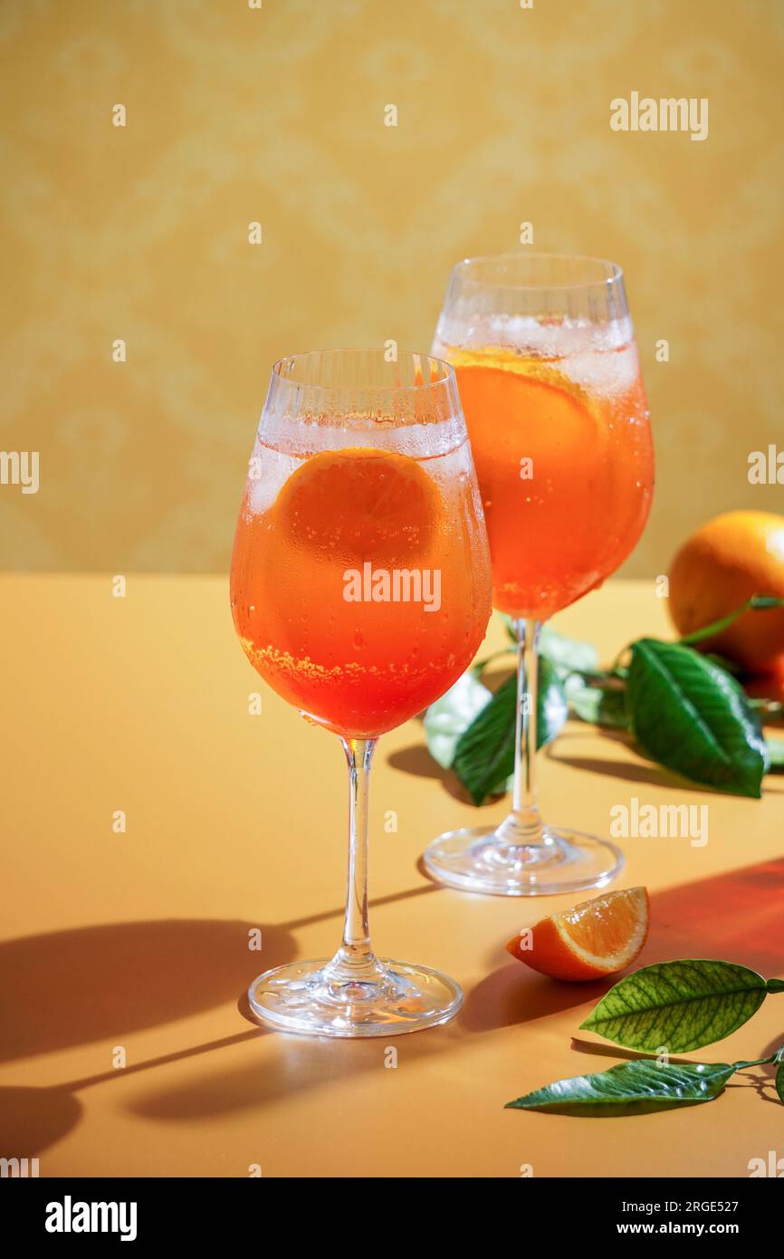 aperol Spritz Cocktail mit Eis, ein nebiges erfrischendes Getränk, auf orangefarbenem Hintergrund, Sonnenlicht, Schatten, ein Sommergetränk in einem Weinglas Stockfoto