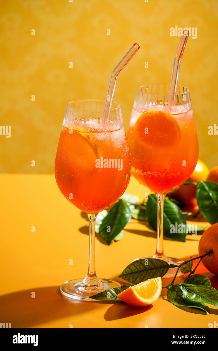 aperol Spritz Cocktail mit Eis, ein nebiges erfrischendes Getränk, auf orangefarbenem Hintergrund, Sonnenlicht, Schatten, ein Sommergetränk in einem Weinglas Stockfoto