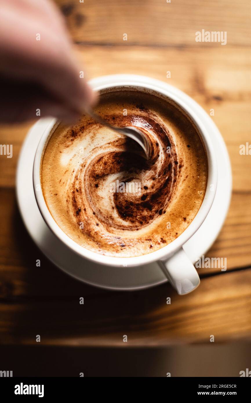 Person, die Kaffee in einer weißen Tasse auf einem Holztisch umrührt Stockfoto