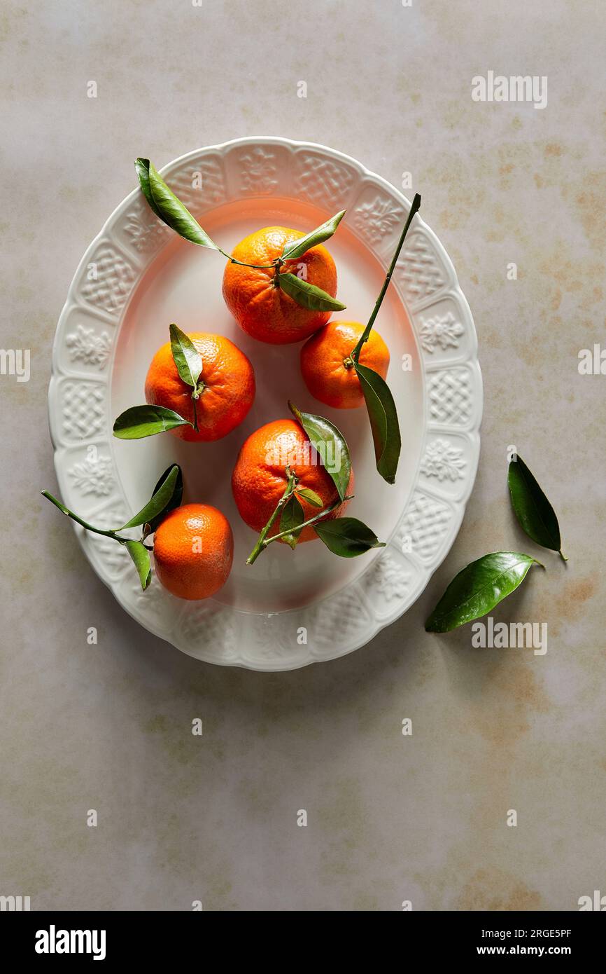 Mandarinenorangen mit Stiel- und Blattdesign auf weißem Teller Stockfoto