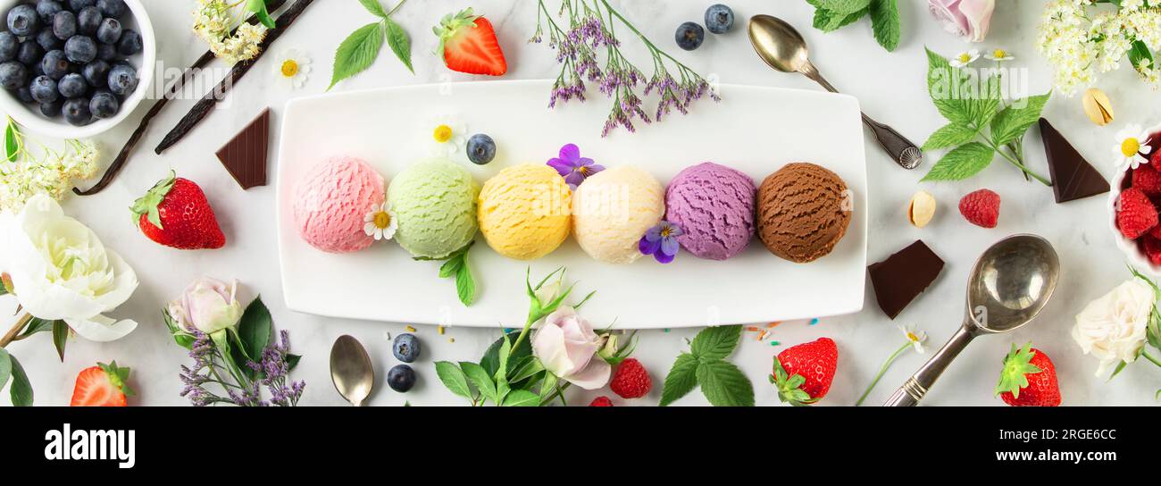 Set aus verschiedenen Eislöffeln und Beeren auf weißem Marmorhintergrund. Erdbeere, Pistazien, Mango, Vanille, Heidelbeere und Schokoladeneis. Oben Stockfoto